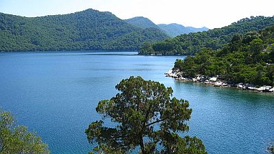 Deep blue salt lake on Miljet surrounded by forested hills.