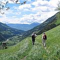 Two people walking on a trail in the italian alps in a lush green spring landscape.