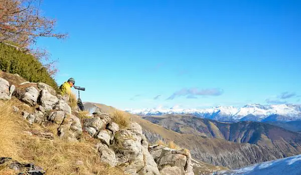 Person with a spotting scope sitting out on a mountain-side, looking out over the French Alps