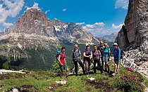 Walkers posing for a photo on a green patch during their walking holiday in the Italian Dolomites, beautiful rock mountains in the background