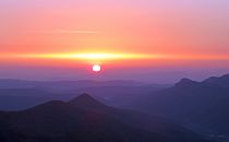 Sun rising from behind a mountain range in reds and oranges