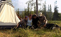 Group of hikers and a dog hugging on a green meadow next to a big tent during their guided walking holiday in Scotland