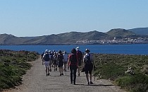 People walking on a wide road; sea, mountain hills and a city in the distance