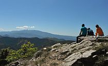 People sitting on a cliff overlooking many low hills