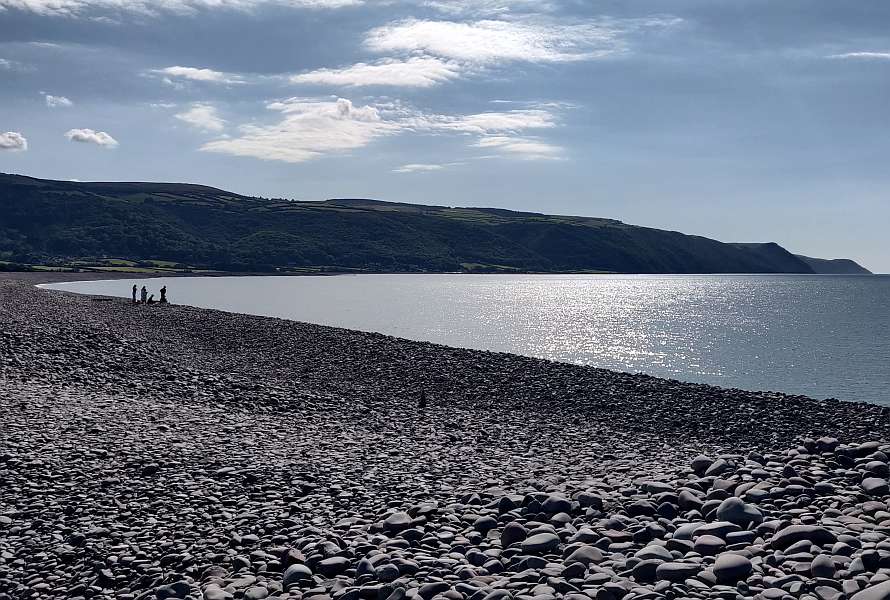 People walking on a stony shore, hills in a distance
