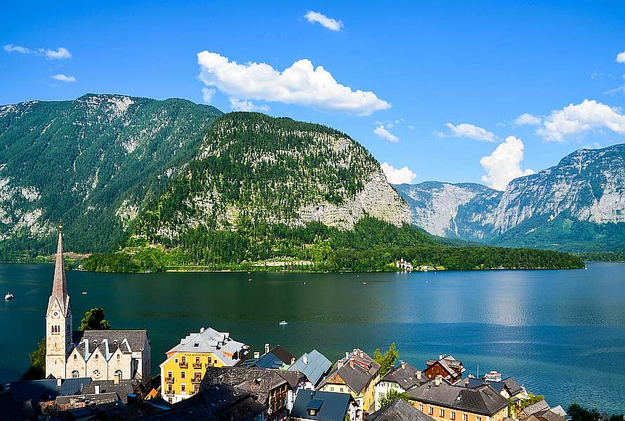Colourful houses in front of a lake, big rocky mountain behind, deep blue sky
