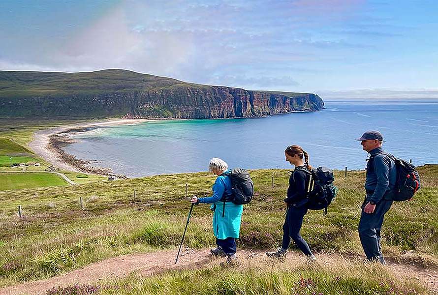 Three walkers on a trail, view of a bay in the distance