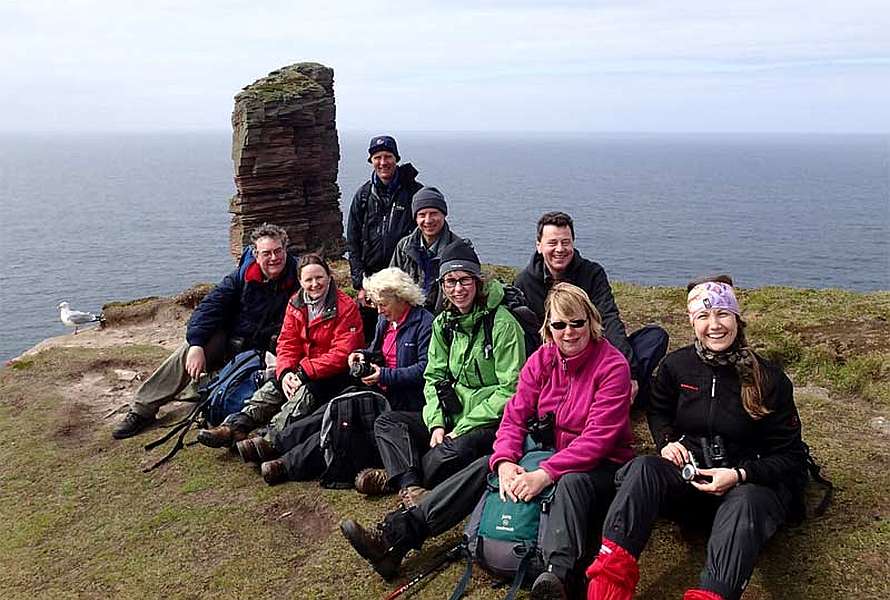 Group of hikers posing for a photo, a rock and the sea in the background