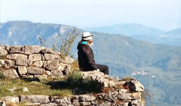 Woman sitting on the edge of a stone wall, overlooking a deep valley