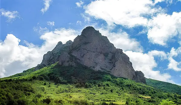 Pointy, rocky mountain-top with lush, green vegetation below it, all under a blue sky with some white clouds