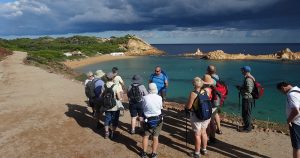 Group of walkers gathered around a man, beautiful turquoise sea and dark sky in the background